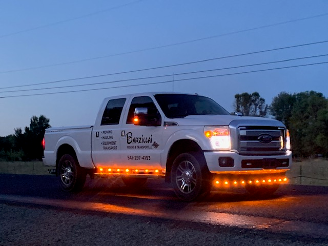 Barzillai Moving & Transport white pickup truck with orange safety lights at dusk, ready for hauling and moving services in Southern Oregon